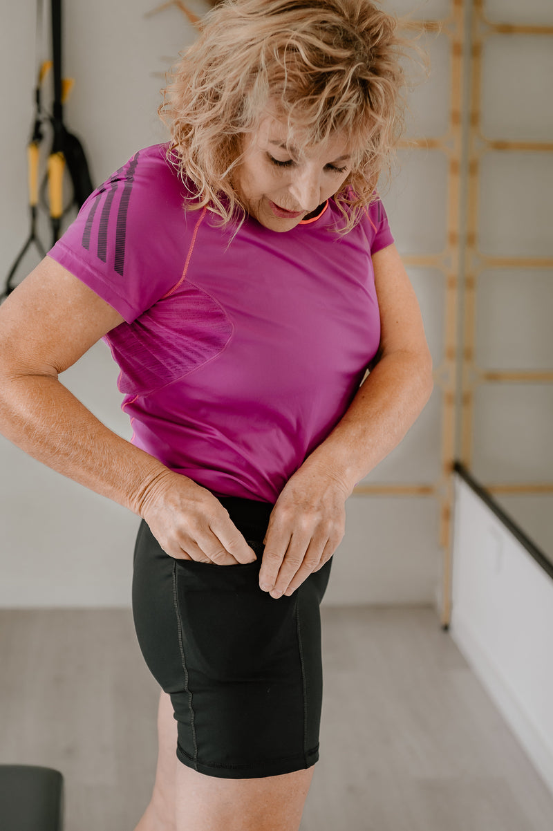 Woman adjusting Phoenix Active Shorts with hip protector shields in a Pilates studio